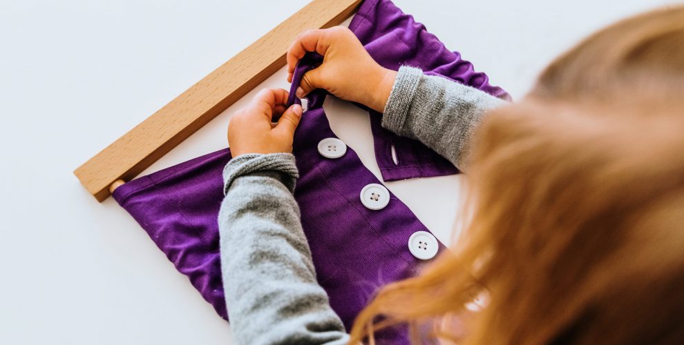 Girl,Buttoning,A,Montessori,Frame,To,Develop,The,Dexterity,Of